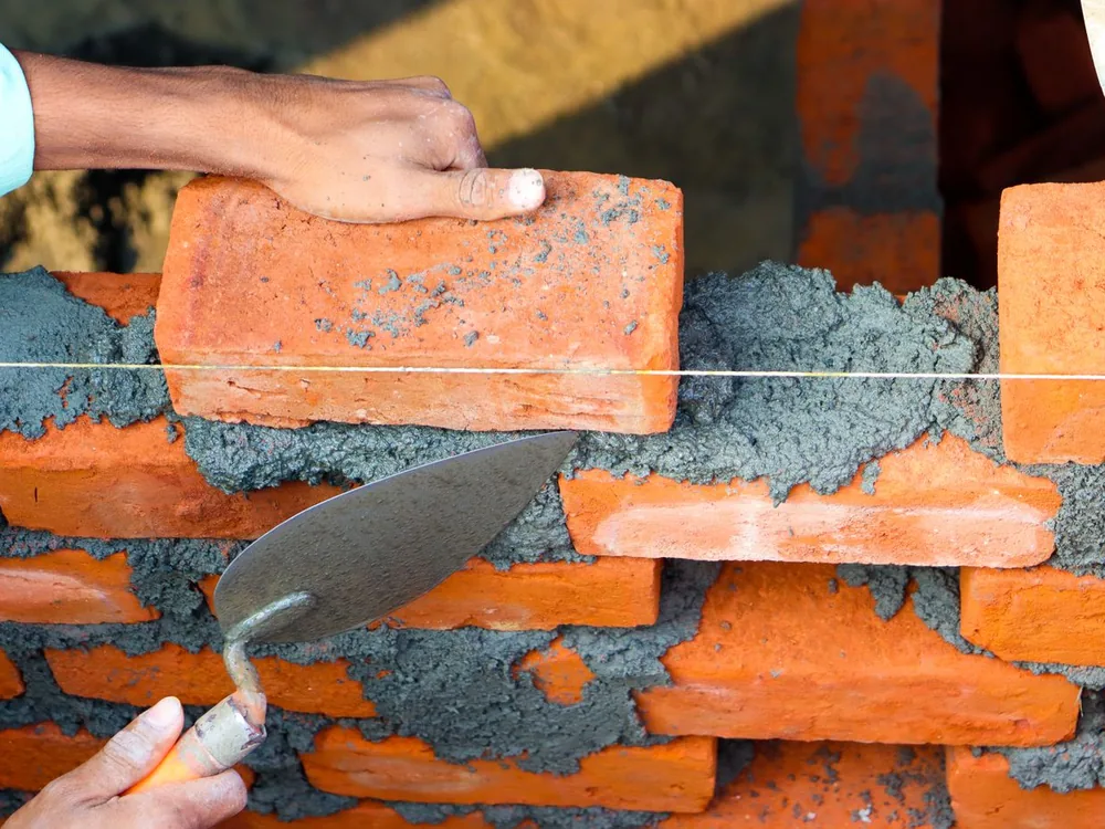 Maçon en train de poser une brique à la truelle sur un mur en construction